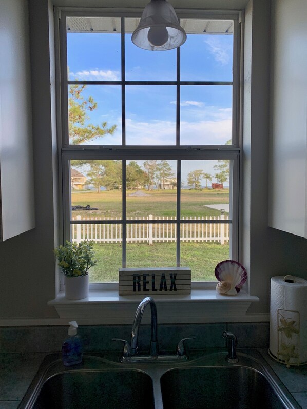 A kitchen with a window, a sink, a potted plant, a 'RELAX' sign, and a view of a fenced yard.