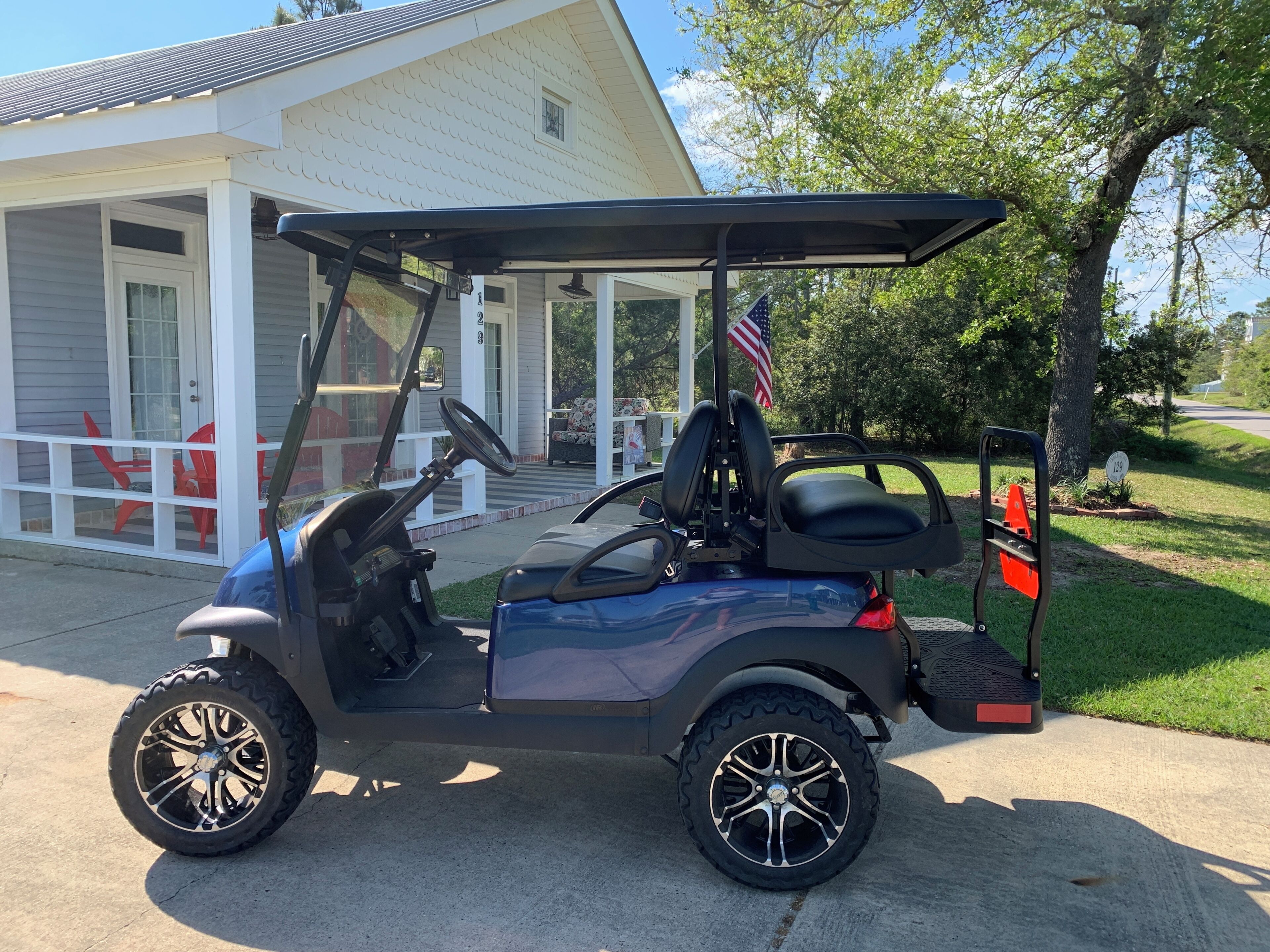 Une voiturette de golf est garée devant une maison qui possède un porche, un drapeau américain et une boîte aux lettres.