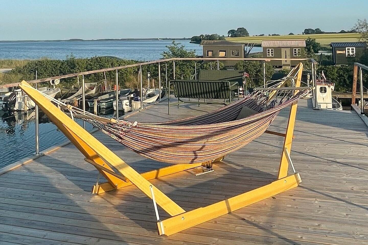A hammock on a wooden deck with a view of the water and houses in the background.