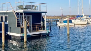 A docked houseboat with a small deck, a staircase, and a railing.