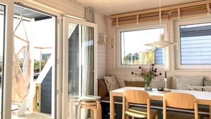 A cozy cabin interior with a dining area, a hammock outside, and a large window providing natural light.