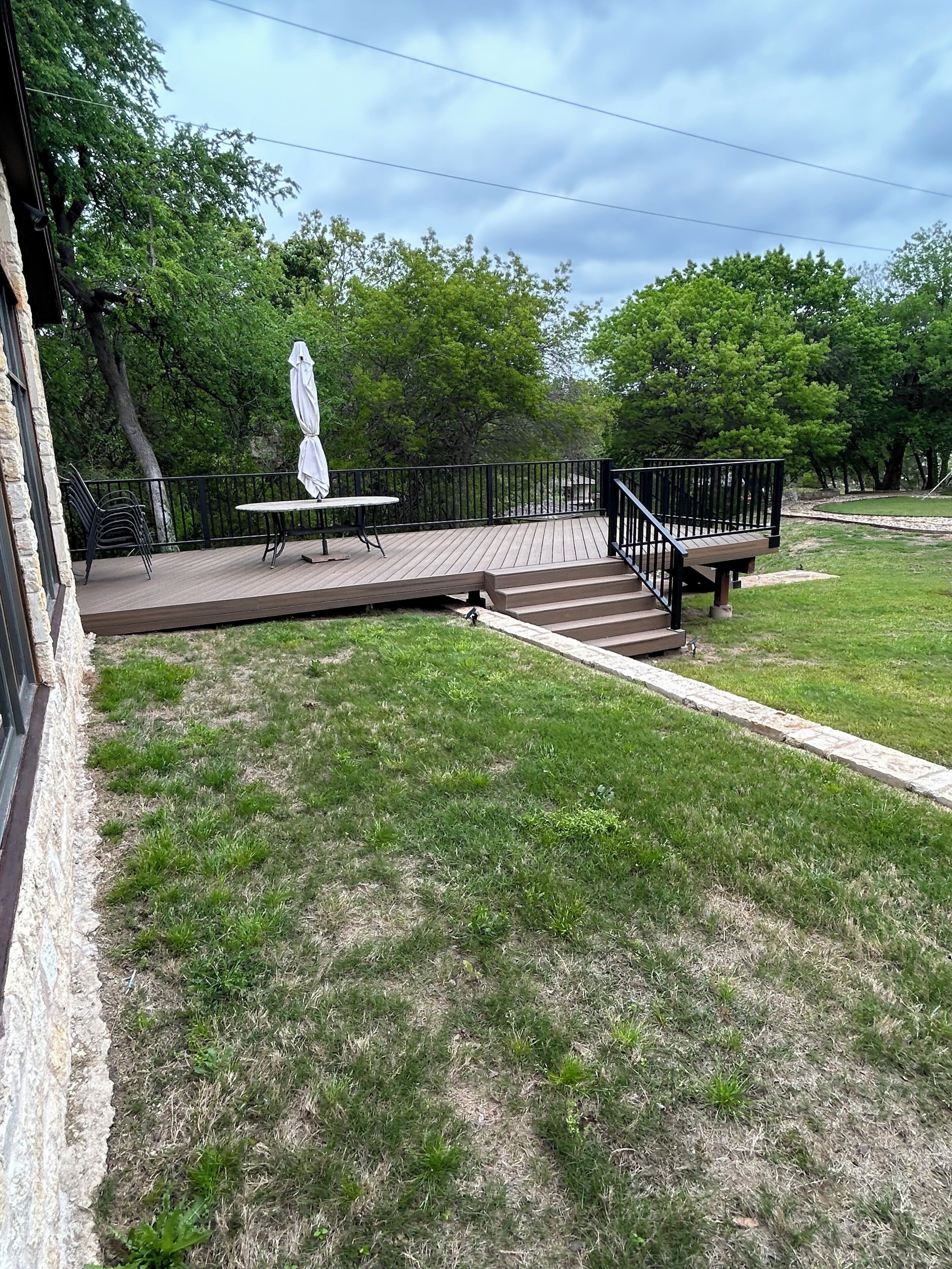 A wooden deck with a table and chairs, surrounded by a stone wall and a grassy lawn.