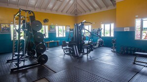 Een fitnessruimte met gewichthefapparatuur, banken en een plafondventilator.
