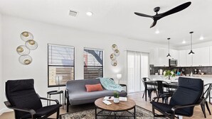 Ein modernes Wohnzimmer mit einer Couch, zwei schwarzen Sesseln, einem Couchtisch und einem Essbereich mit Tisch und Stühlen.