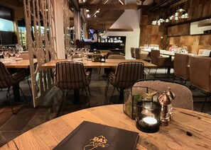 En restaurantindretning med træborde, stole og en bar i baggrunden.