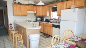 Une cuisine avec des meubles de rangement en bois, un réfrigérateur blanc, un four à micro-ondes et une cuisinière. On y trouve des tabourets en bois et une table avec un set de table.