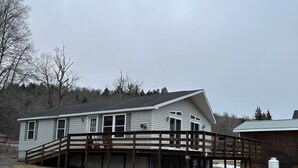 Une maison à deux étages dotée d’une terrasse en bois, d’un porche couvert et d’un espace clôturé.