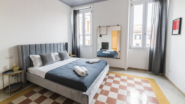 A modern bedroom with a checkered floor, a bed with a grey headboard, and a nightstand. - Vintage Apartment Giuliana (Rome)