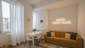A modern living room with a white table, a mustard-colored sofa, and a neon sign reading "ROMA CAPUT MUNDI". - Vintage Apartment Giuliana (Rome)