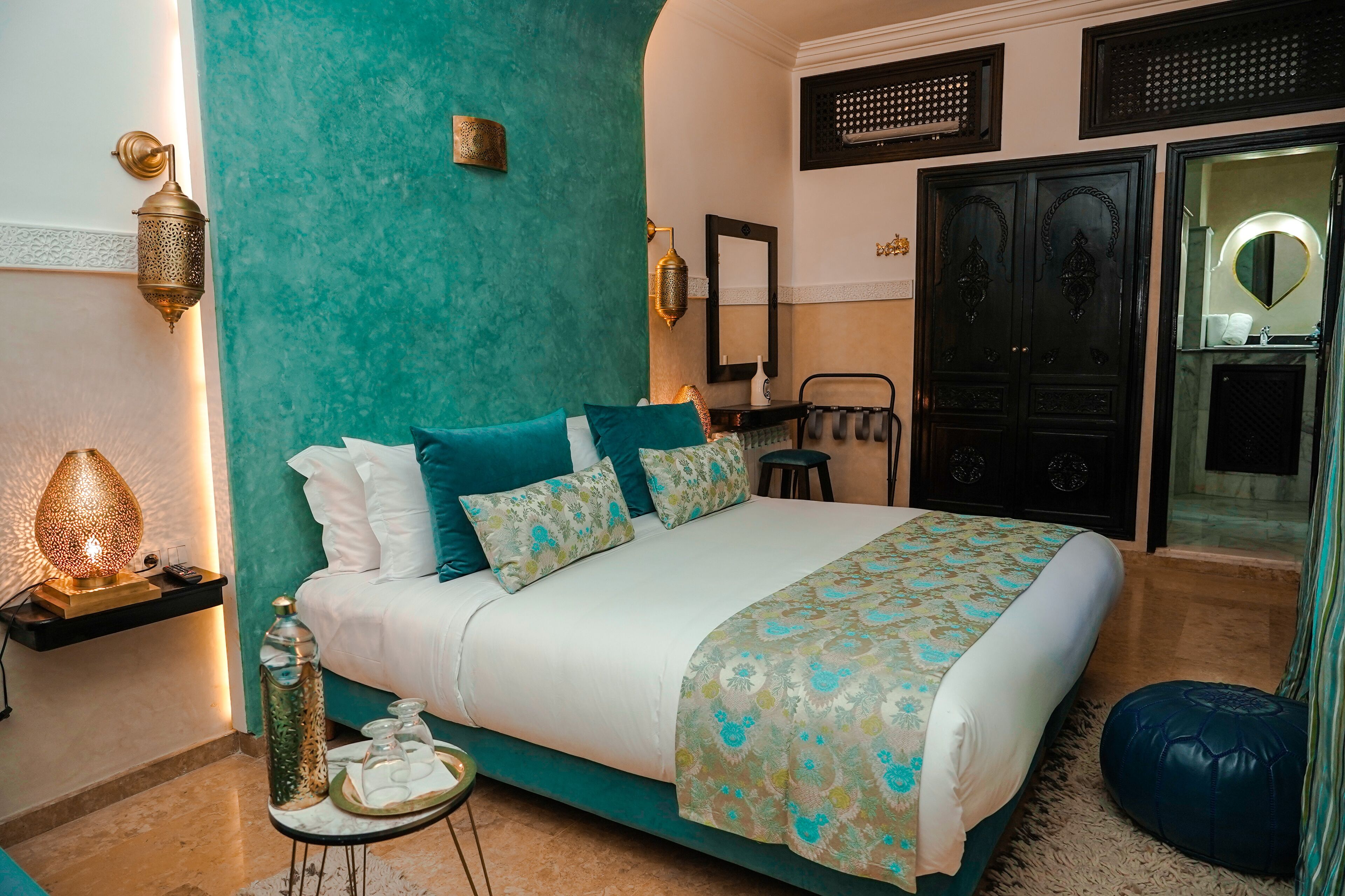 Une chambre avec un mur d’accent de couleur turquoise, un lit avec une literie à motifs, une table de chevet avec une lampe et un miroir au-dessus du lit.