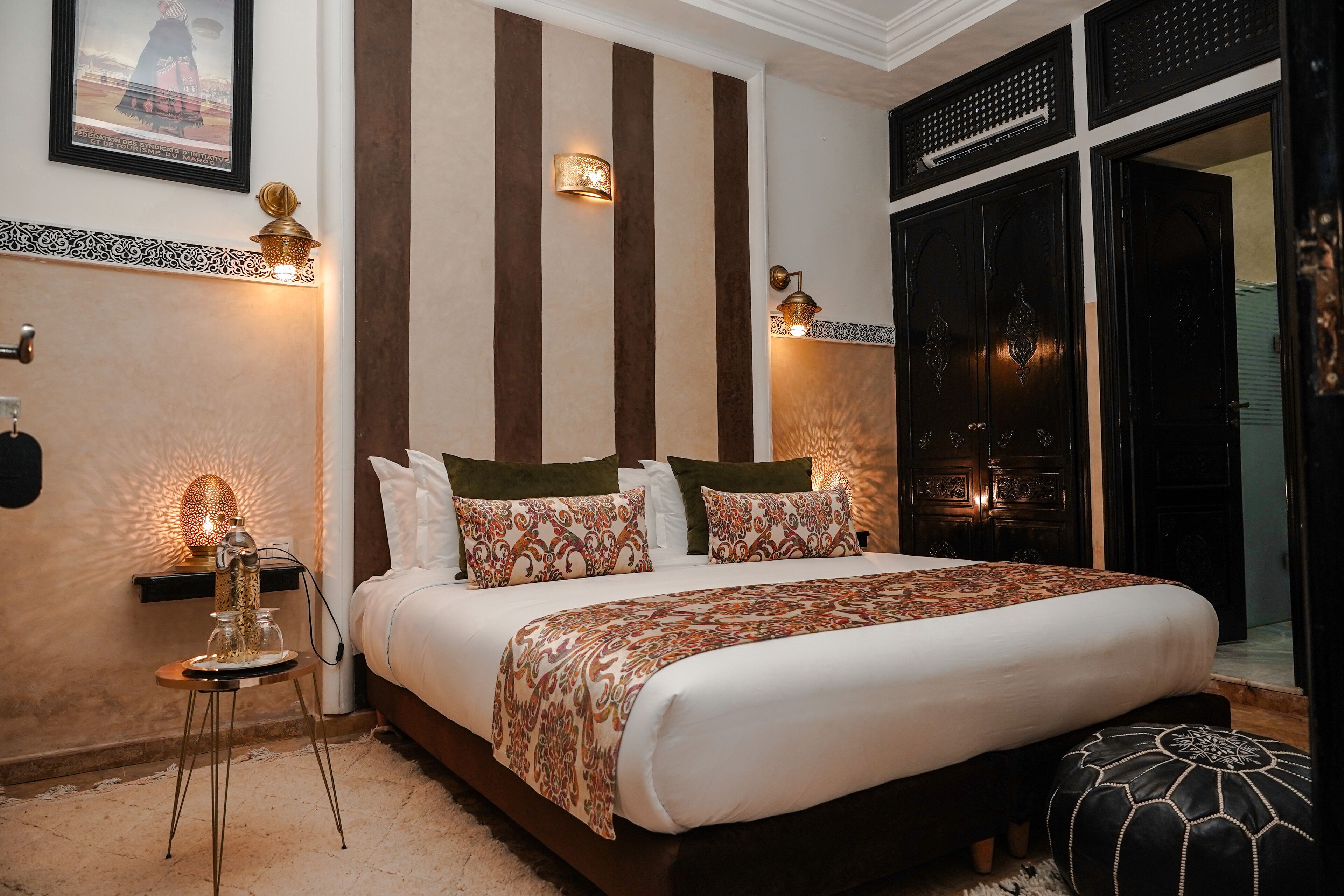 A bedroom with a large bed, decorative wall sconces, a small side table, and a large window with a view.