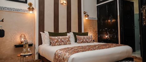 A bedroom with a large bed, decorative wall sconces, a small side table, and a large window with a view.