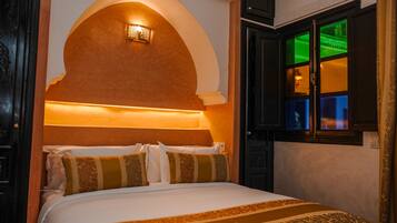 Habitación de hotel con una cama grande, un muro curvo con una lámpara y una ventana con vistas a un paisaje verde.