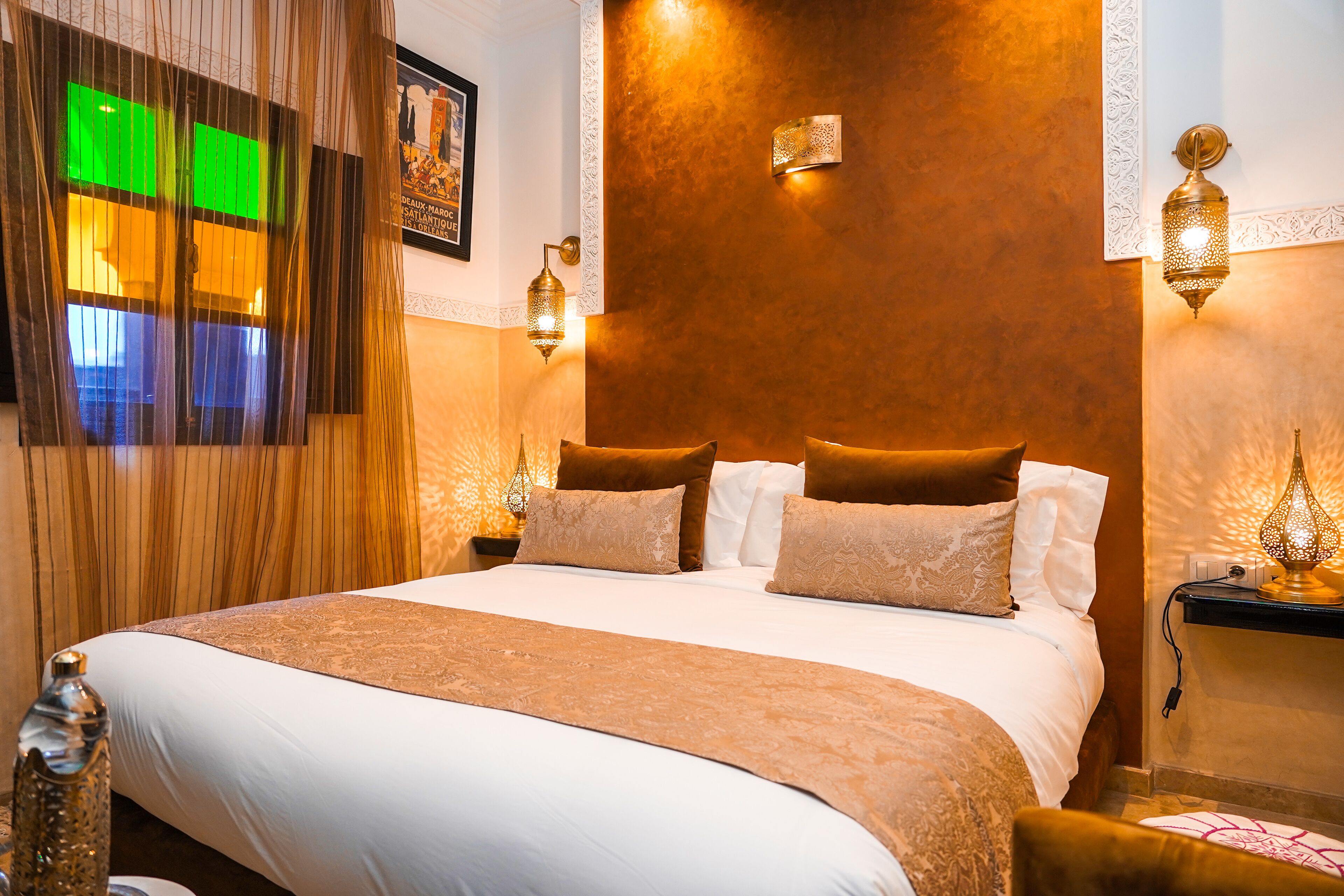 A neatly made bed with a brown bedspread and white linens, two bedside lamps, and a wall-mounted light fixture.