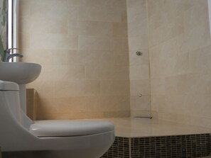 Un bagno con un water, un lavabo e una doccia con pareti piastrellate.