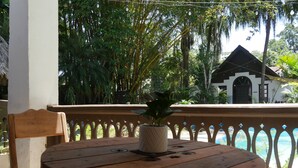 A wooden table with a potted plant, a chair, and a balcony railing with a view of a building and trees. - Hotel Mandacaru Puerto Viejo (Cahuita)