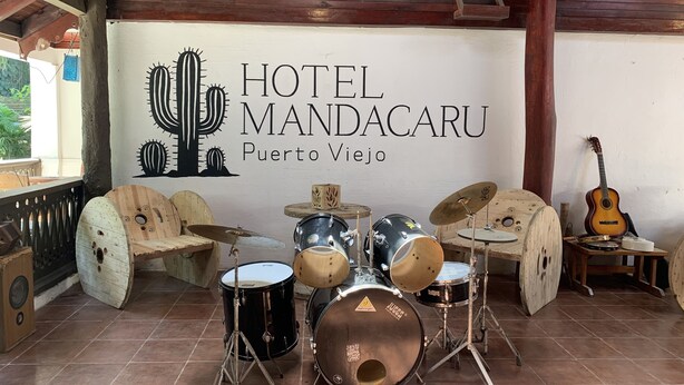 A drum set in a room with a wooden ceiling and a sign for Hotel Mandacaru in Puerto Viejo. - Hotel Mandacaru Puerto Viejo (Cahuita)