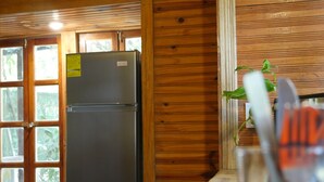 A kitchen with a refrigerator, wooden cabinets, and a window with a view of greenery. - Hotel Mandacaru Puerto Viejo (Cahuita)