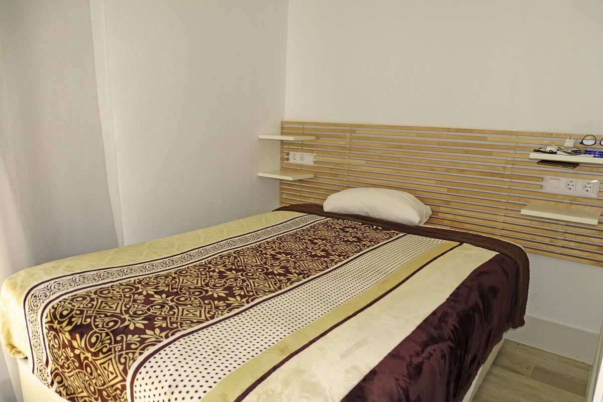A single bed with a patterned bedspread, a wooden headboard, and a bedside table with a lamp.