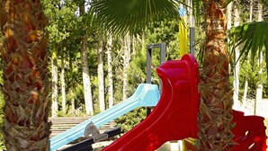 Un parque infantil con un tobogán rojo y uno azul, rodeado de palmeras.
