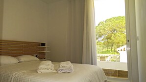 Un dormitorio con cama, cabecera de madera, ventana con cortinas y vistas a la vegetación.