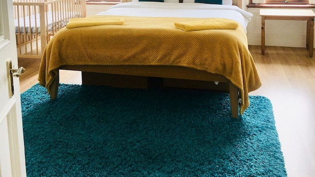 A bedroom with a bed, a wooden headboard, a blue rug, and two windows. - VS-Entire Flat-Central Scotland-Falkirk| Self-Check-in |Pet-friendly | Parking (Falkirk)