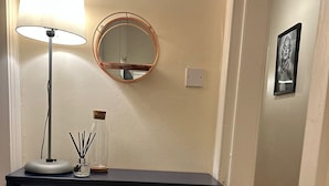 A room with a dark blue cabinet containing white mugs and plates, a lamp, and a mirror. - VS-Entire Flat-Central Scotland-Falkirk| Self-Check-in |Pet-friendly | Parking (Falkirk)