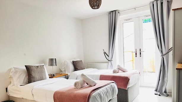 Hotellihuone, jossa on kaksi sänkyä, pieni pöytä, lamppu ja näkymä ulos.