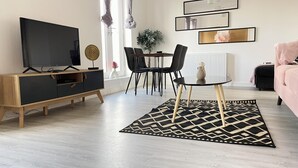 Moderni olohuone, jossa on televisio, mustat tuolit, pyöreä pöytä ja kuviollinen matto.