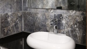 Un baño con un lavabo blanco, paredes de mármol oscuro y un espejo grande.