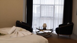 Una habitación de hotel con una cama, dos sillones, una mesita redonda y cortinas translúcidas.