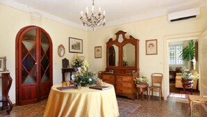 A room with a round table covered in a yellow cloth, a wooden cabinet, a large mirror, and a chandelier. - Cozy and comfort Villa in the Lucca surroundings (Capannori)