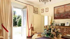 A room with a large window, a chandelier, a table with a floral arrangement, and a painting on the wall. - Cozy and comfort Villa in the Lucca surroundings (Capannori)