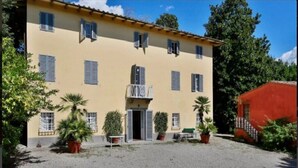 A two-story building with a yellow facade, multiple windows with shutters, and a gravel driveway. - Cozy and comfort Villa in the Lucca surroundings (Capannori)