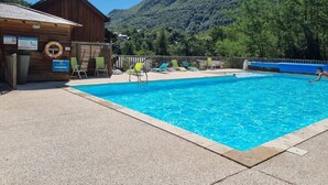 Ein Schwimmbecken mit Liegestühlen, ein Holzbau und eine Bergkulisse.