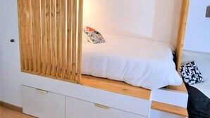 Ein Etagenbett mit Holzlattung, einer weißen Matratze und einem Nachttisch mit Schubladen.