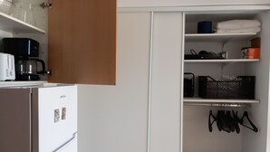 Cocina compacta con refrigerador, cafetera y microondas. Hay un gabinete de almacenamiento con estantes que contienen varios objetos.