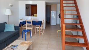 Un espacio habitable compacto con sofá, mesa de comedor, sillas, mesa de centro, lámpara, refrigerador y escalera de madera.