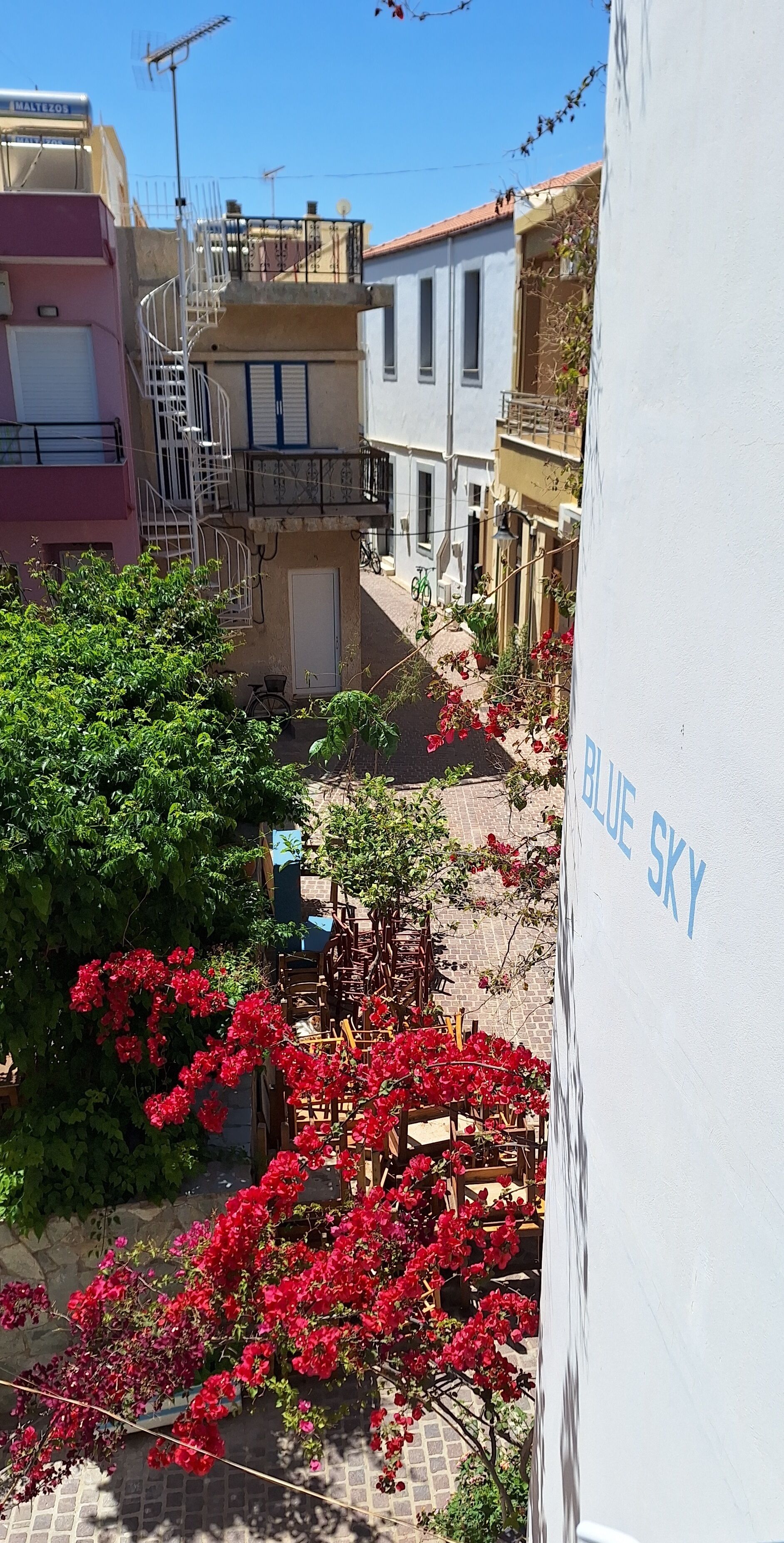 Un quartier résidentiel avec un immeuble blanc portant l’inscription « BLUE SKY » et un immeuble rose doté d’un escalier.