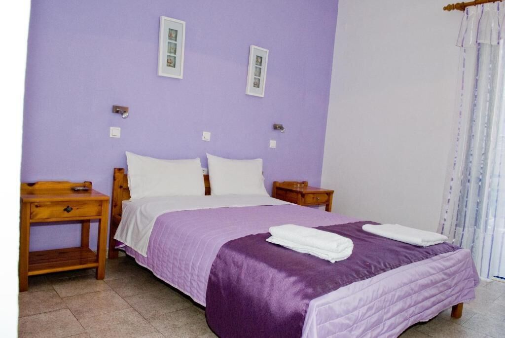 A single bed with a purple bedspread and white pillows in a room with purple walls.