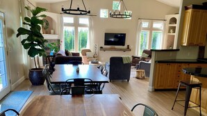 Een ruime woonkamer met een houten eettafel, zachte zithoeken, een grote kamerplant en een televisie.