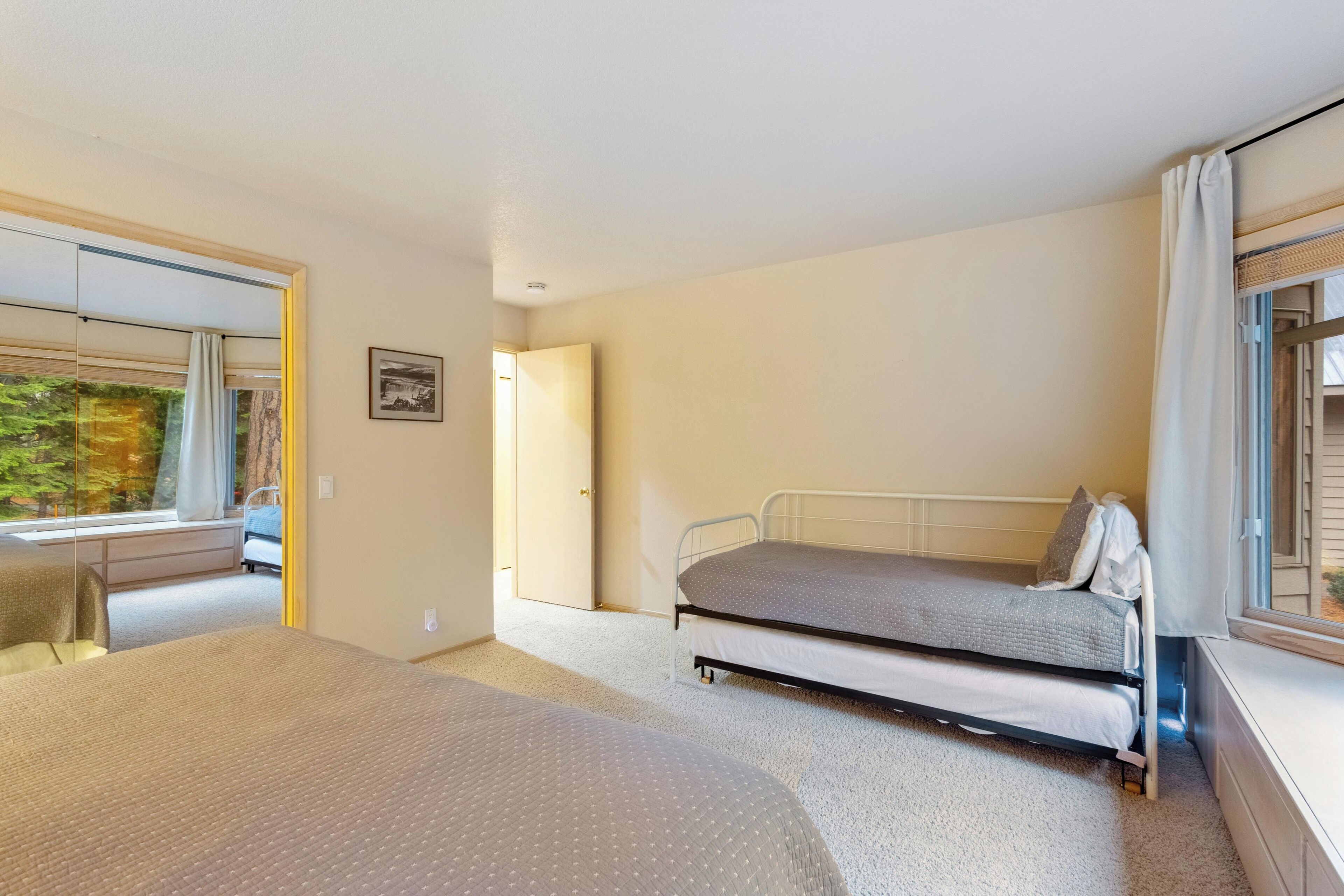 A bedroom with two beds, a window with curtains, a door, and a framed picture on the wall.