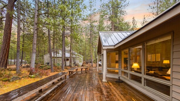 Une terrasse en bois avec des bancs, un bâtiment à structure vitrée et un paysage boisé en arrière-plan.