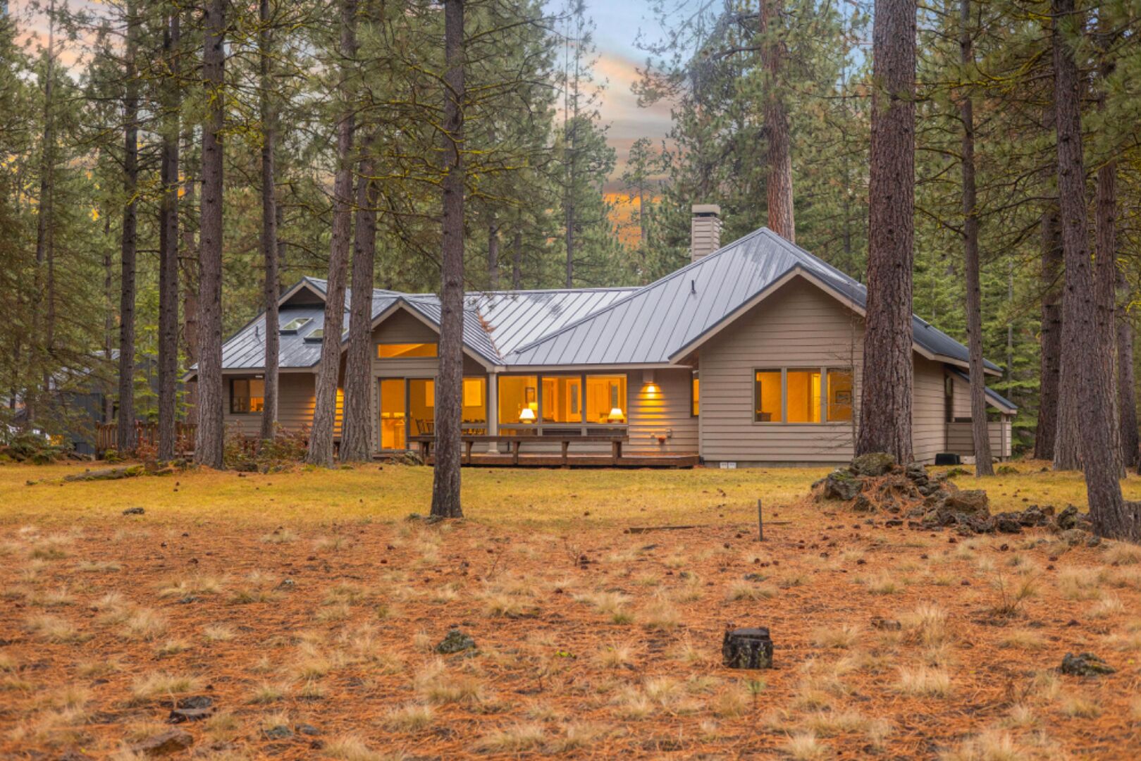 A cabin with a large porch, surrounded by tall pine trees.