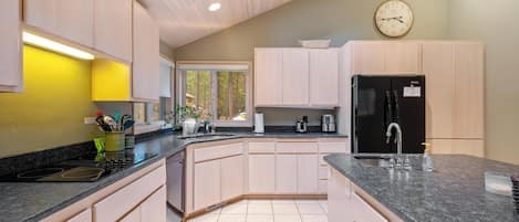 Una cocina moderna con armarios de colores claros, un refrigerador negro y un ventanal con vistas a árboles.
