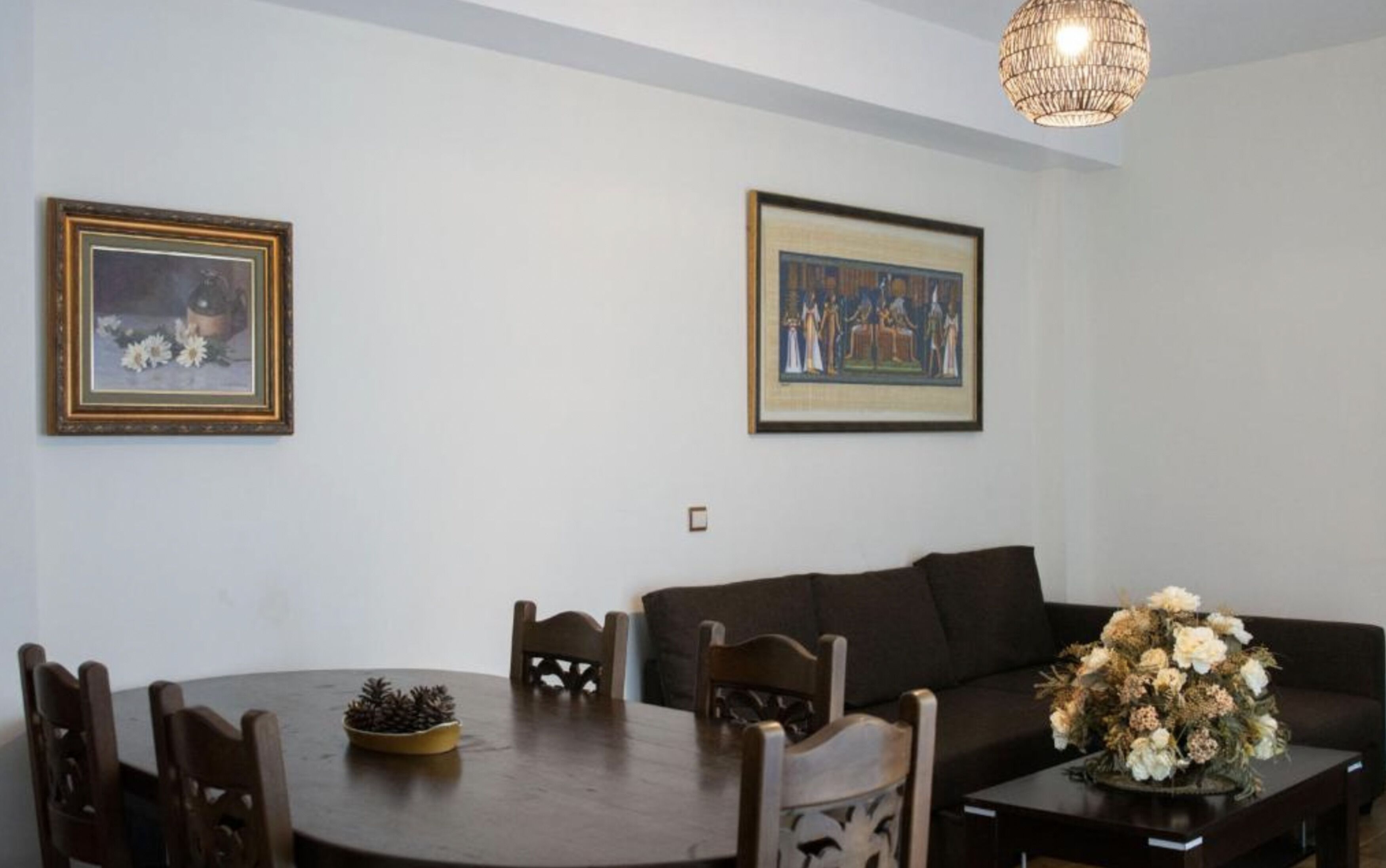 Zona pranzo con tavolo rotondo, sedie, un divano e due opere d'arte appese al muro.