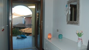 A hotel room with a sliding glass door leading to a balcony, a white dresser, a mirror, and a vase with flowers. - Holiday home (Villasimius)