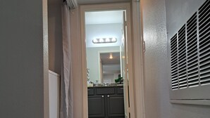 Un couloir avec un sol carrelé, un luminaire au plafond et une grille d’aération sur le mur.