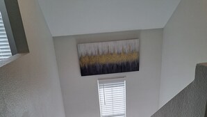 Un escalier aux murs blancs et à la finition texturée, menant à un palier doté d’une fenêtre et d’un élément décoratif mural.