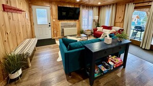 A wooden-paneled room with a sofa, a coffee table, and a television. - Stylish Mountain Retreat: Hot Tub, Fire Pit, Whiteface Views! (Wilmington)
